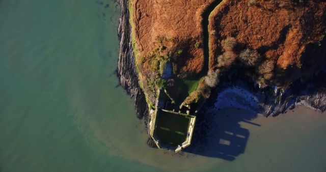 This breathtaking aerial photo captures a deserted historic structure perched perilously on the edge of a cliff, overlooking the lush green sea. Depicting an interesting blend of nature and decay, the sturdy, weather-beaten architecture speaks of a time long past. Ideal for use in travel blogs, historical articles, nature documentaries, or architectural reviews. It evokes a sense of adventure and discovery, making it perfect for tourism promotions and educational content.