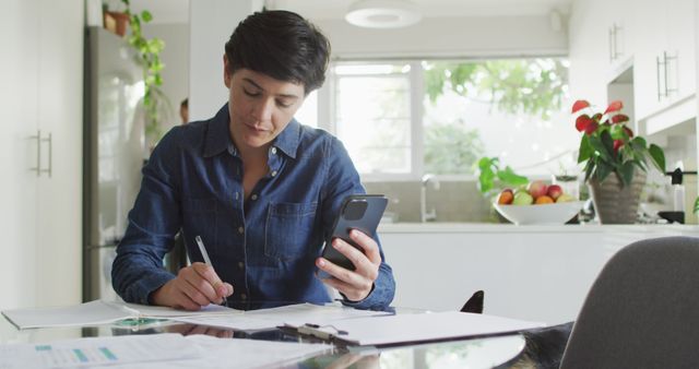 Caucasian woman taking notes and calculating finances using smartphone at home. family finance and budget concept