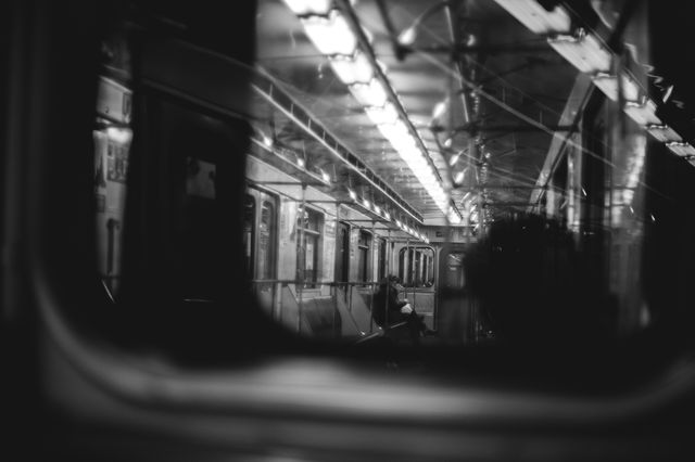 Black and white interior of subway car showing reflections and lights casting shadows. Ideal for blog posts, artistic projects, and depictions of urban life, solitude, and public transportation.