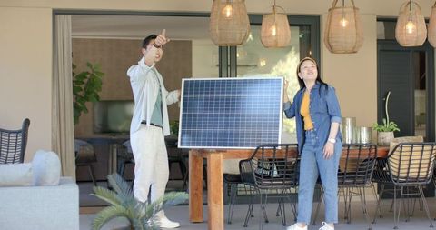 Asian couple inspecting solar panel on covered patio table under rattan pendant lights