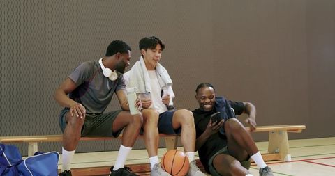 Diverse male friends laughing and sharing phone while packing gym bags on bench