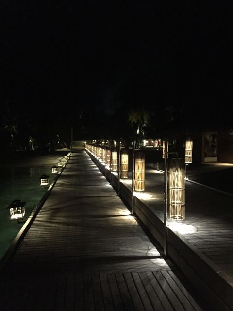 Nighttime wooden boardwalk lit by lanterns creating serene tropical atmosphere, perfect for travel advertisements, vacation rentals, and tourism brochures emphasizing relaxation and scenic beauty.