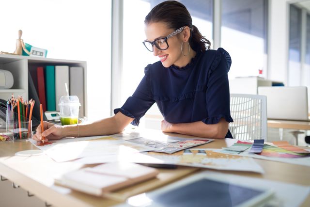 Female executive working at her desk in a modern office, drawing and organizing files. She looks focused and professional, likely engaging in creative or design work. Perfect for depicting women in business, modern workspaces, productivity, and creative industries.