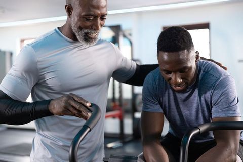 African american trainer guiding client on air bike, intense cardio coaching in gym