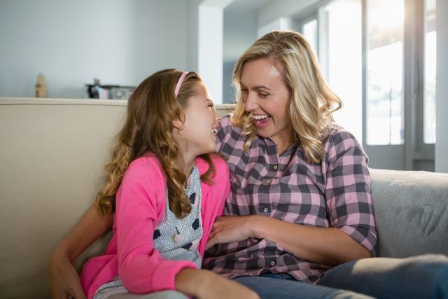Mother and daughter sharing a joyful moment on the couch, perfect for family-oriented content, parenting blogs, advertisements promoting family values, and lifestyle articles.