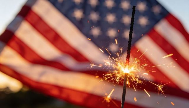 Handheld sparkler lighting against american flag at sunset for fourth of july celebration