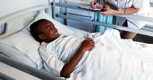 Child in hospital bed smiling while receiving care from nurse with clipboard in medical setting. Ideal for healthcare advertisements, hospital websites, patient recovery stories, and pediatric care awareness campaigns.