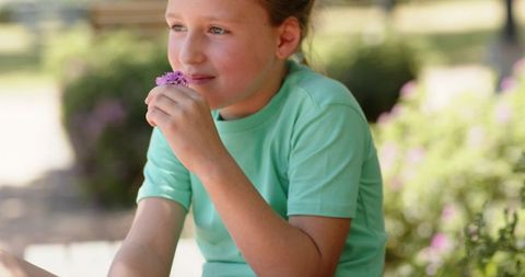 Girl smelling purple flowers in garden wearing mint green t-shirt