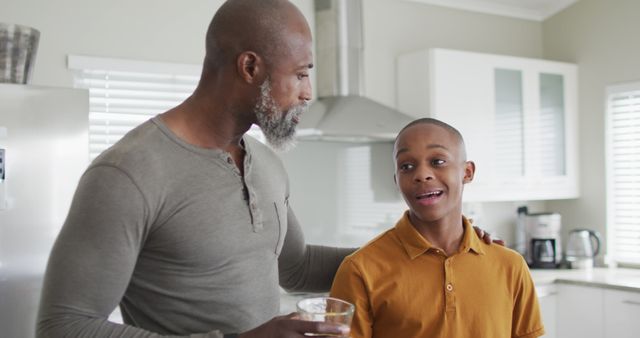 Father bonding with teenage son in modern kitchen. Perfect for content about parenthood, family relationships, modern living, and parenting advice. Useful in blogs, family-oriented websites, social media posts, and advertisements promoting family time.