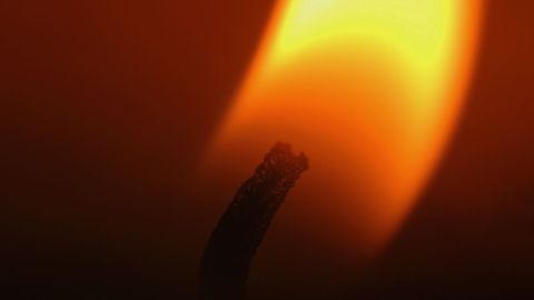 Macro candle wick glowing within tall orange flame for moody ambience and ritual