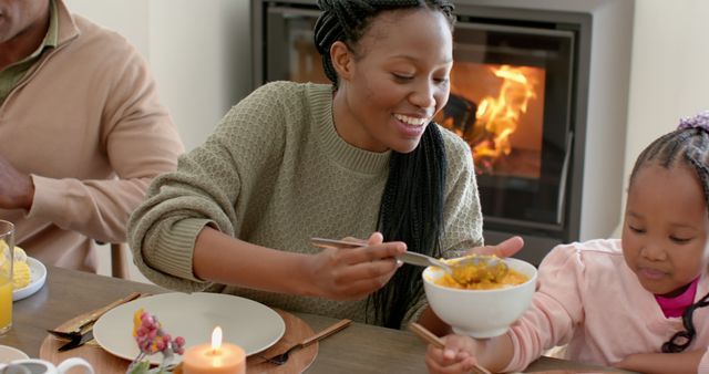 Smiling family gathered around table enjoying Thanksgiving meal by fireplace. Use this for holiday promotions, family-themed content, or advertisements depicting togetherness and gratitude.
