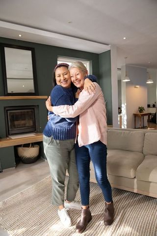 Mature friends hugging in cozy living room, warm embrace and joyful companionship at home