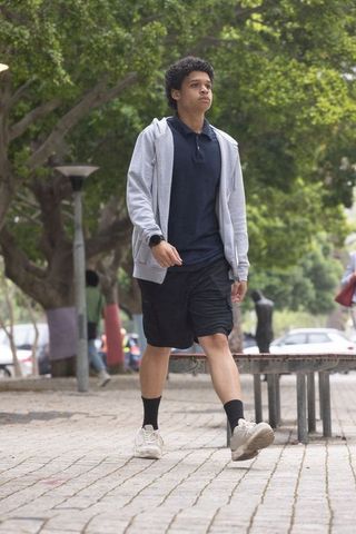 Young african american man walking in urban park wearing gray hoodie and sneakers
