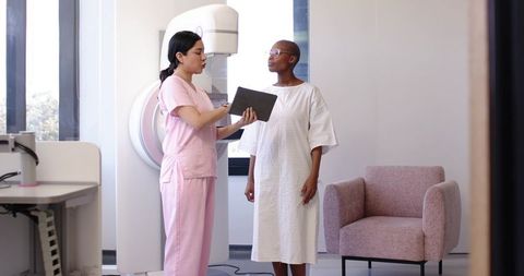Medical nurse explaining mammogram procedure to African American patient in clinic room