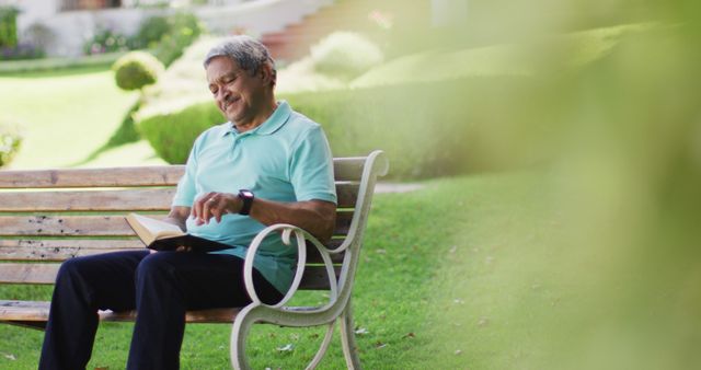 Image of happy biracial senior man reading book and sitting on bench in garden. active retirement lifestyle, hobby and spending time outdoors.