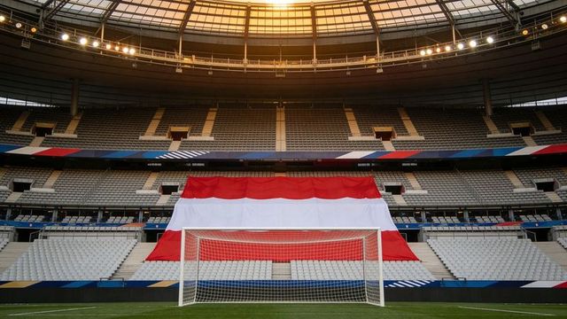 Red-and-white flag draping central stands behind white soccer goal in stadium arena