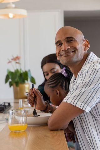 Smiling father enjoying morning breakfast with diverse family at modern kitchen island