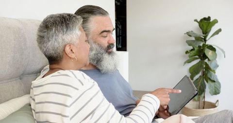 Senior Couple Relaxing on Bed Using Tablet for Leisure