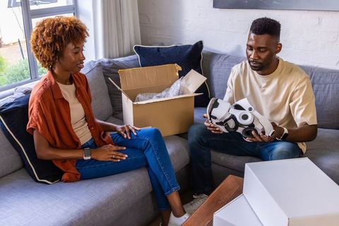 African american couple unboxing and inspecting new smart home robot on living room sofa