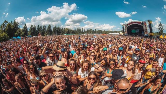 Packed festival crowd cheering at outdoor main stage on sunny blue-sky day