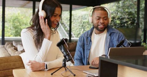 Diverse co-hosts recording podcast in bright home studio with headphones and laptop