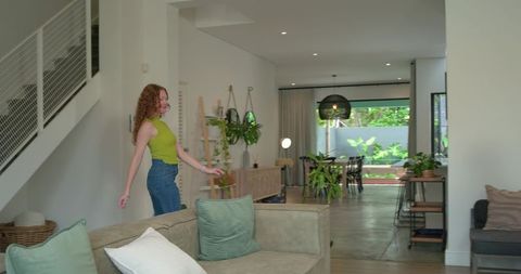 Young woman walking through modern living room with plants wearing casual denim outfit