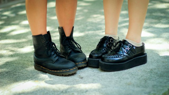 Close-up of two people wearing black platform shoes and boots on pavement outdoors. Ideal for use in fashion blogs, shoe store advertisements, street style articles, and social media fashion promotions.