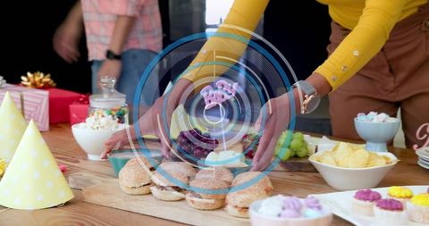 Woman arranging sliders on festive snack table with party hats and colorful desserts