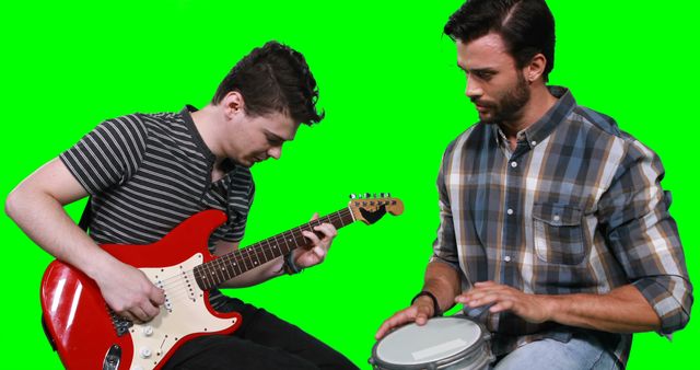 Male musicians singing song while playing guitar and drum against green screen