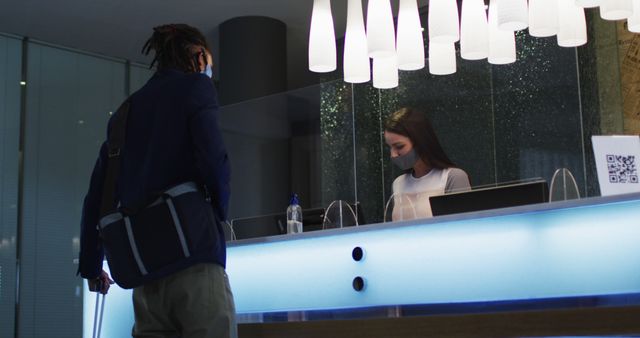 Biracial man and female receptionist wearing face masks at hotel reception desk. out and about during coronavirus covid 19 pandemic.