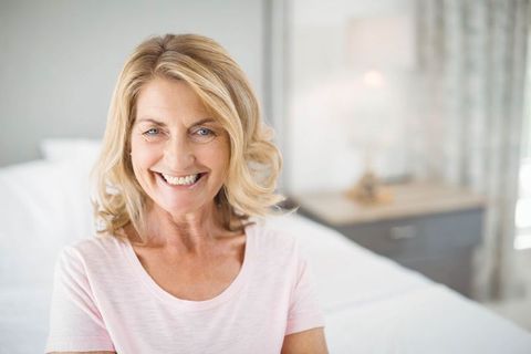 Smiling Senior Woman Sitting on Bed in Calming Bedroom