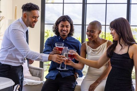Multiracial team toasting with champagne in bright modern living room celebrating success