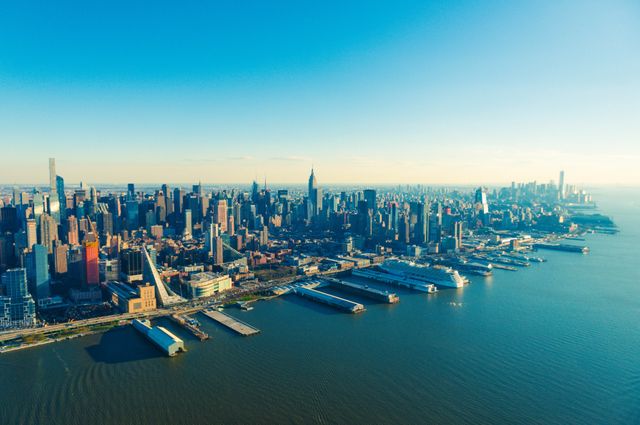 Aerial view captures expansive Manhattan skyline with its iconic skyscrapers and waterfront bays beneath a hazy blue sky. Ideal for websites and projects emphasizing urban development, travel, architecture, and New York City's vibrancy. Suitable for use in travel blogs, city planning presentations, tourism advertisements, and architectural portfolios.