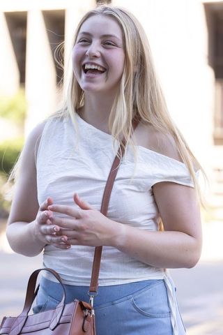 Laughing blonde woman in off-shoulder white top and denim with brown crossbody bag