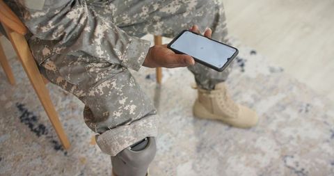 Veteran wearing camouflage holding smartphone and showing prosthetic knee sitting indoors