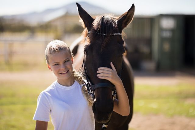 Young girl smiling and embracing a horse at a ranch on a sunny day. Ideal for use in content related to outdoor activities, animal companionship, equestrian sports, rural lifestyle, and youth leisure activities.