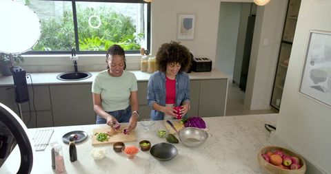 Diverse women preparing colorful vegetable bowls at modern kitchen island with ring light