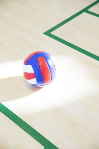 Red white blue volleyball resting on polished hardwood court spotlight casting shadow
