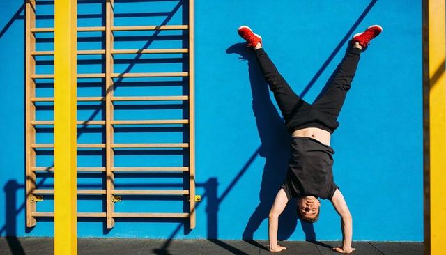 Young man performing handstand on urban fitness wall, vibrant blue backdrop with yellow bars