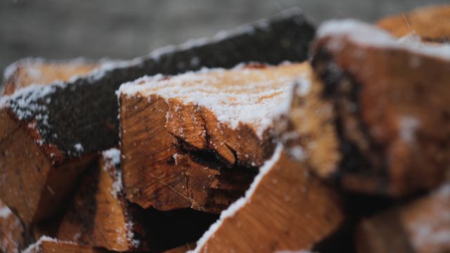 Close-up view of freshly chopped firewood with a light dusting of snow, showcasing a wintery atmosphere. Ideal for use in outdoor adventure content, winter preparation articles, firewood supplies advertisements, or winter-themed storytelling.