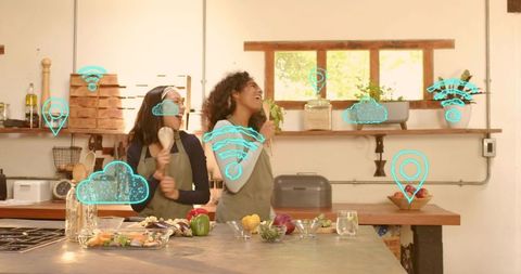 Laughing women cooking together using augmented reality icons in sunlit modern kitchen