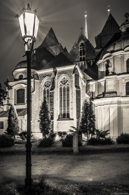 Depicting a vintage street lamp illuminating a gothic church at night, this image captures historical architecture with an eerie atmosphere. Illuminated against the night sky, it suggests a quiet, old city vibe. Suitable for projects focusing on history, heritage, European medieval architecture, and atmospheric themes in photography.