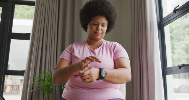 Image of plus size african american woman in sport clothes putting on smartwatch. active healthy lifestyle, exercising at home.