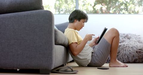 Young Asian Man Using Tablet on Living Room Floor