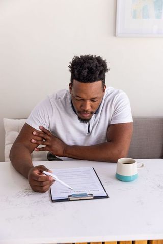 African american man reviewing paperwork at home holding pen and teal coffee mug, modern