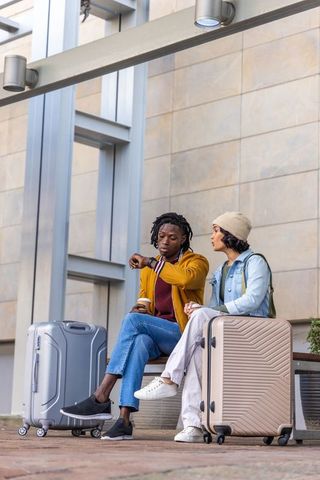 Diverse travelers waiting on urban bench checking watch with suitcases and coffee