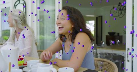 Laughing woman leading multigenerational tea gathering with cake at sunlit modern home