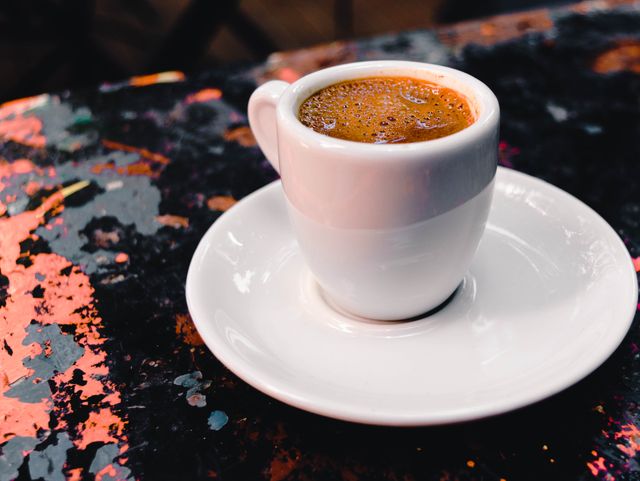 Espresso cup with saucer placed on a rustic table in a café setting. Perfect for use in coffee shop promotions, caffeine-related articles, lifestyle blogs, café menu design, and social media content highlighting cozy coffee moments.