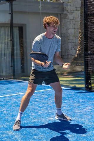 Smiling young man playing padel on bright blue court holding racket