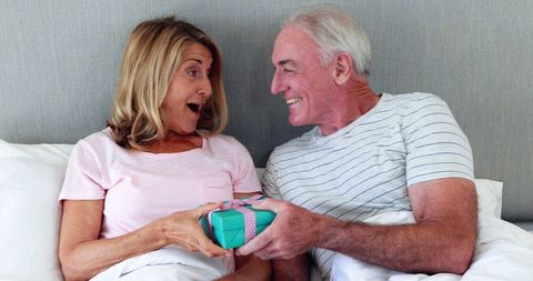 Senior Couple Sharing Gift in Bedroom with Surprise and Joy